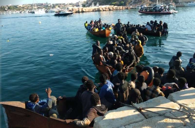 fila di barchini carichi di migranti al molo di lampedusa